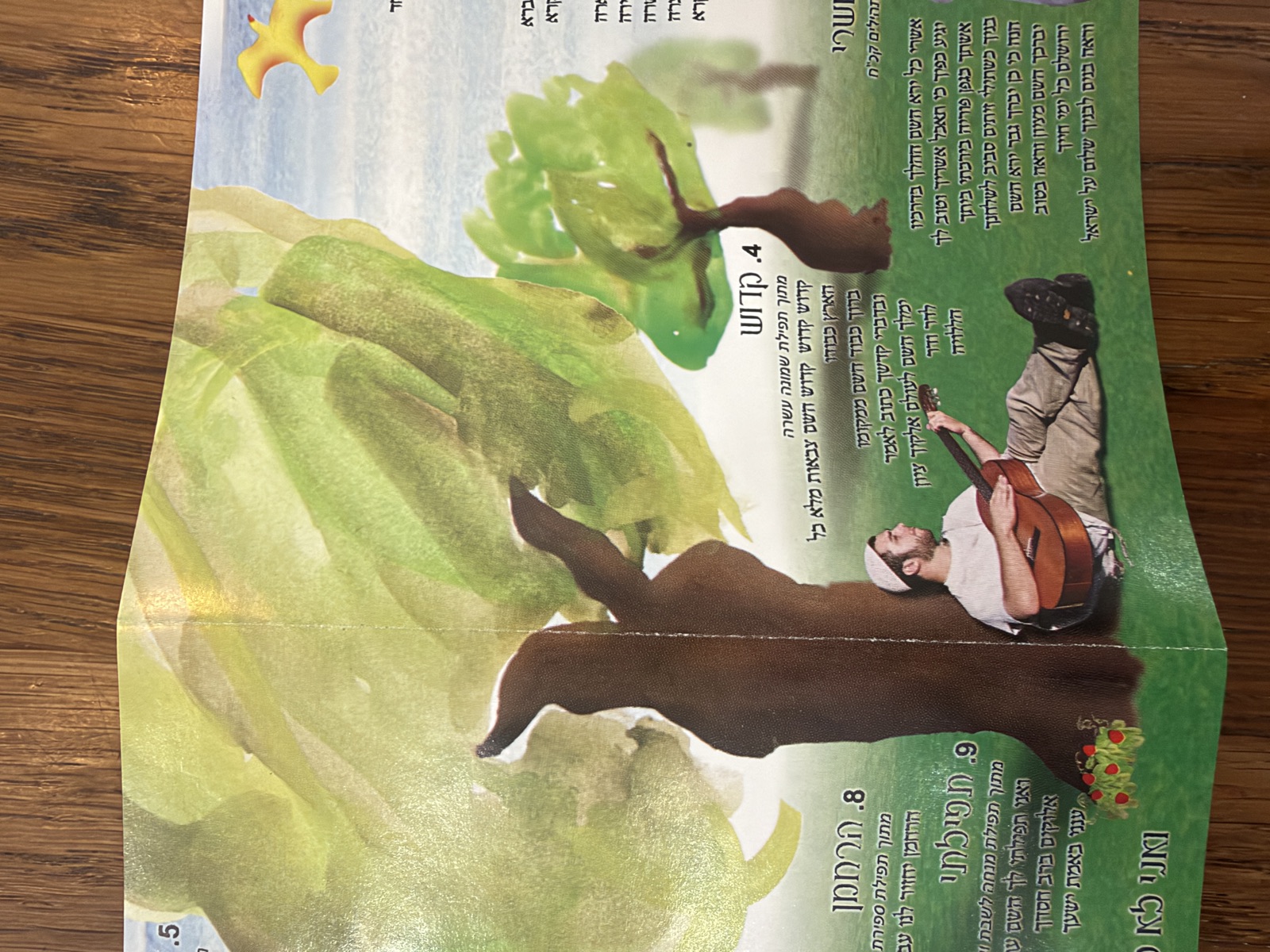 Booklet spread with Hebrew lyrics over watercolor trees